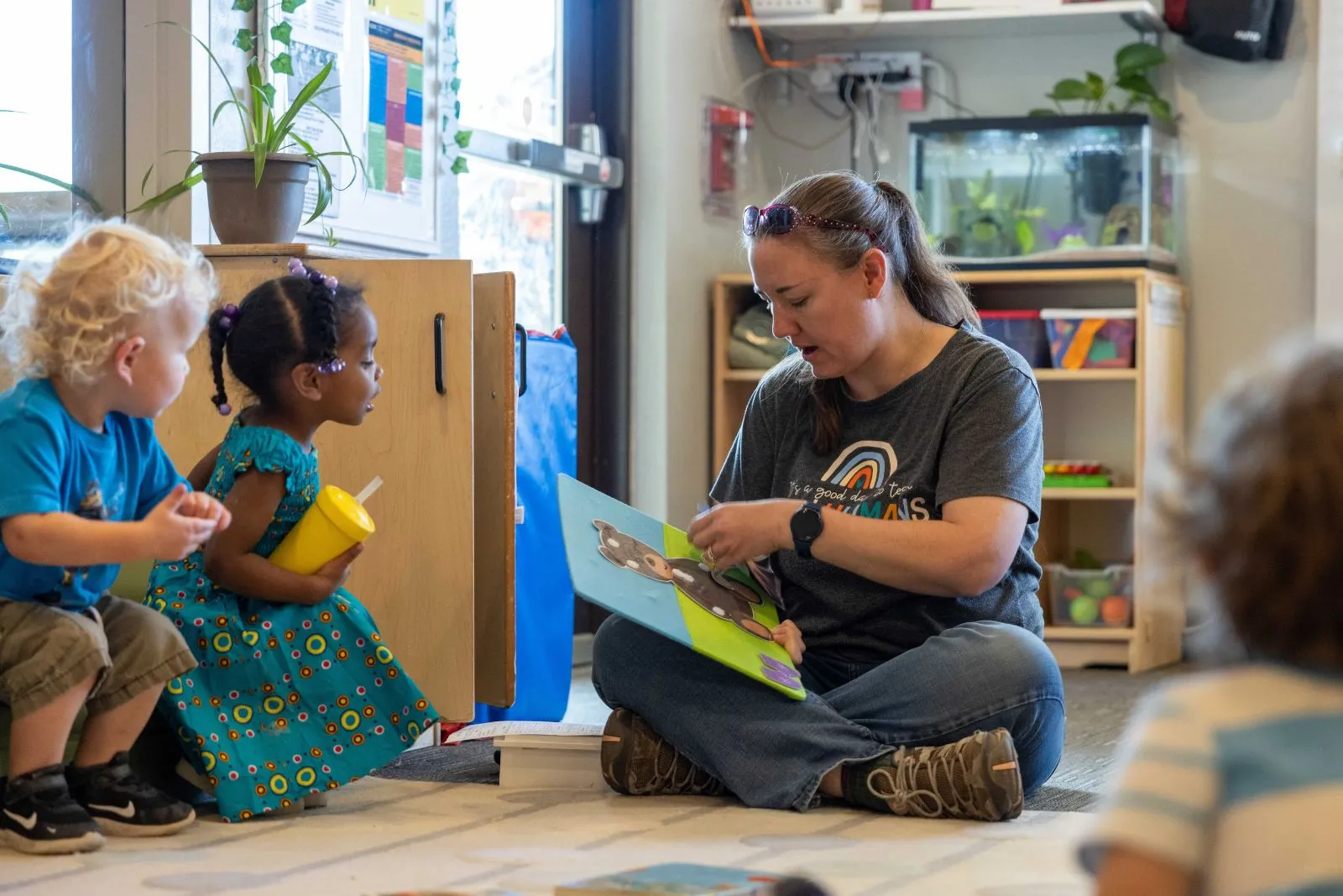 A teacher reading to children sitting on the ground